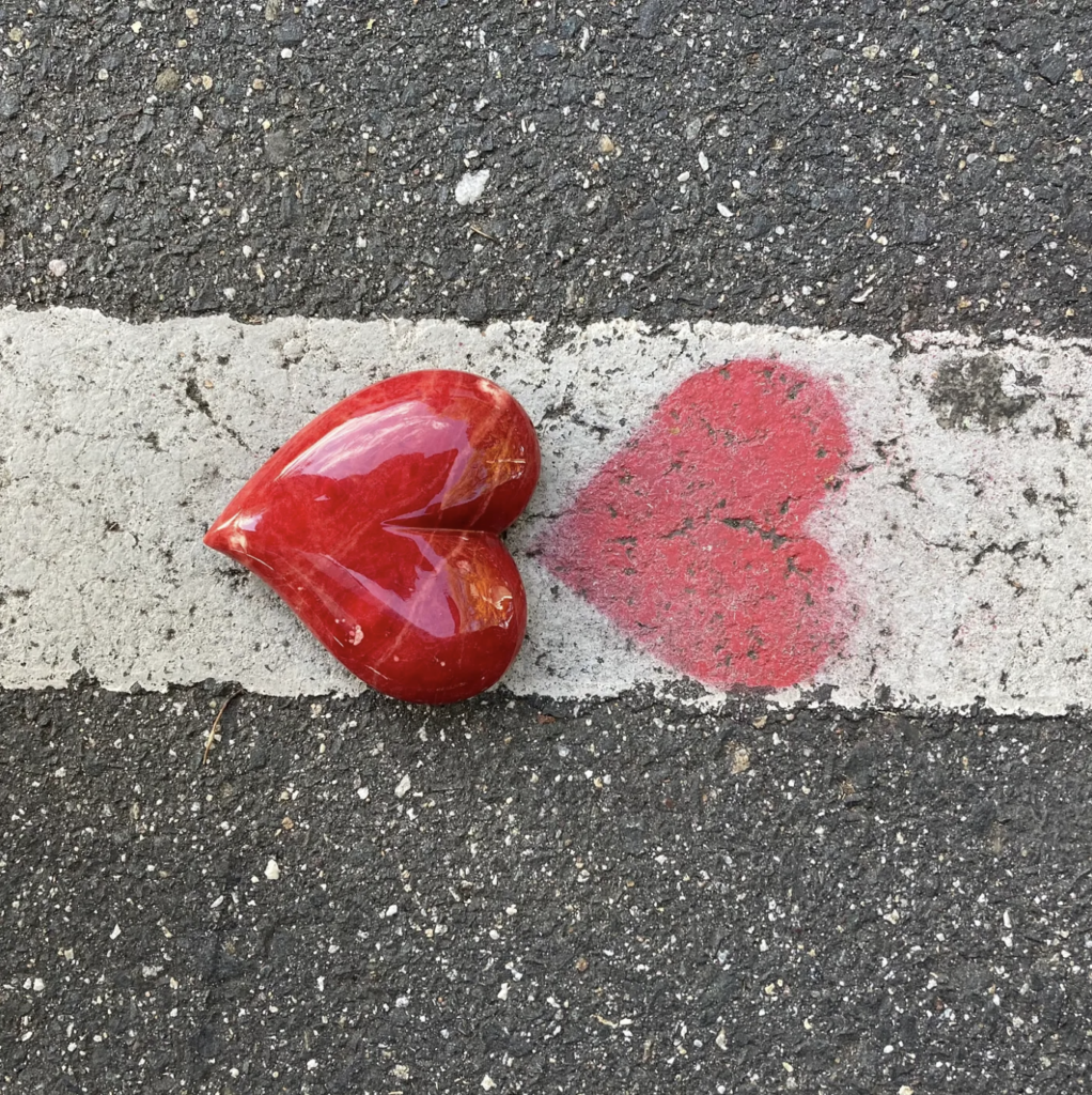 red marble heart by red painted heart on a white stripe on a paved street